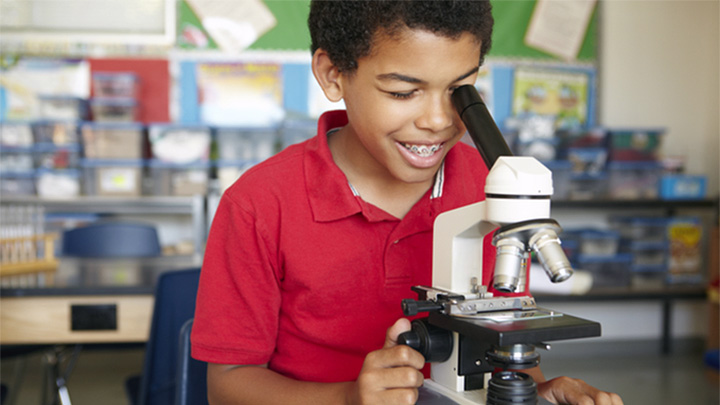 A child looking down a microscope in a school classroom.