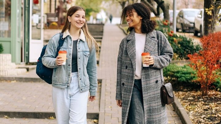 Two students walking together carrying take-out coffees.