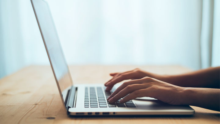 A close-up of a person's hands typing on a laptop keyboard.