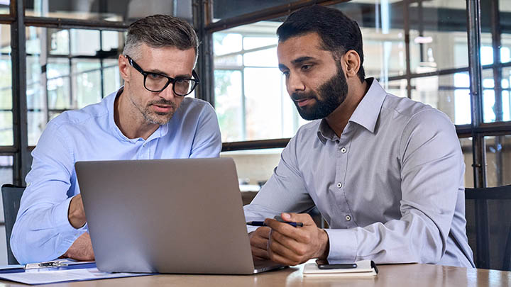 A consultant sitting with a client, discussing information displayed on a laptop.