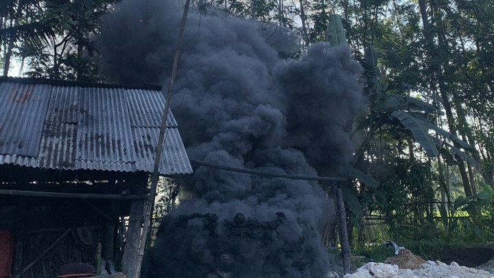 An Indonesian man sits in a hut while a fire burns nearby.