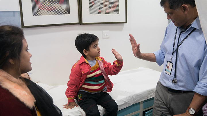 Professor Vaskar Saha high-fiving a small Indian child in a hospital.