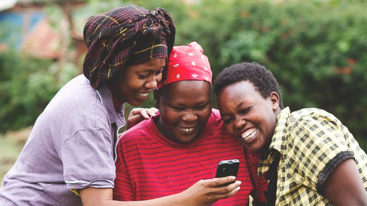 A group of three African women laughing together at content on a mobile phone.