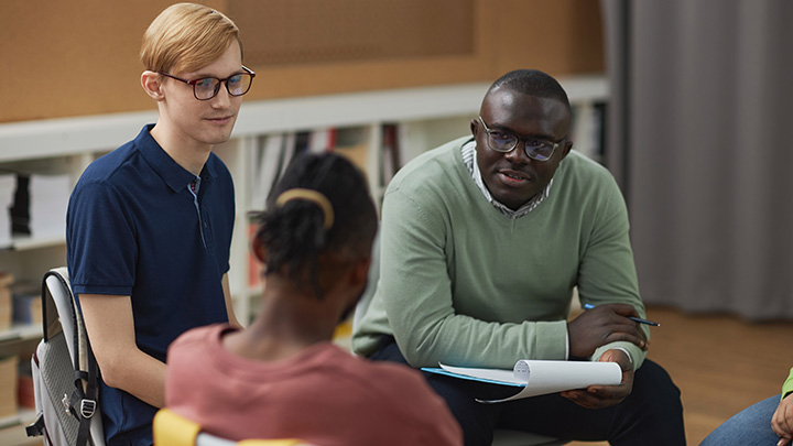 Portrait of black man as male psychologist talking to group teenagers in therapy session