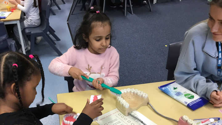 Primary school children learning about teeth cleaning with a dental student.