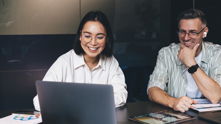 A young woman at a laptop with a man sitting next to her. Both are smiling.