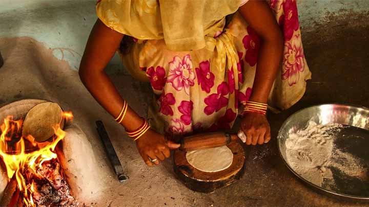 An Asian woman rolling out chapatis next to a cooking fire