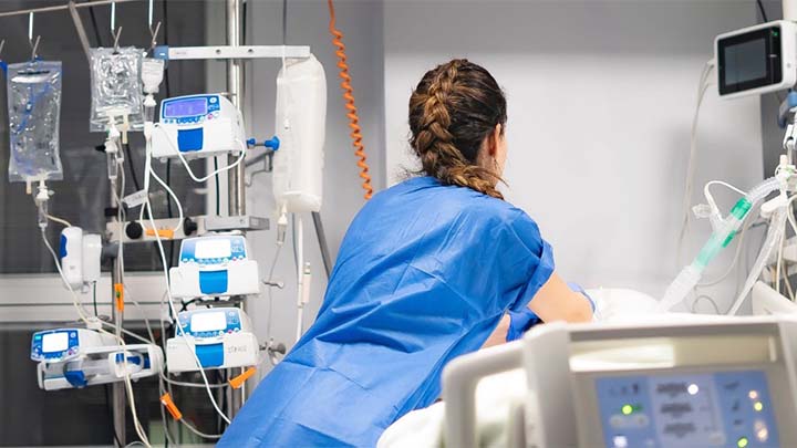 A clinician in a blue uniform, tending to a patient in a hospital ward.