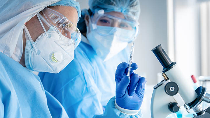 Two researchers in lab, one holding a test tube with a microscope in front of them