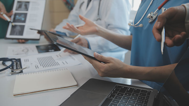 Three people working together in a clinical setting, looking at a computer and tablet screens.