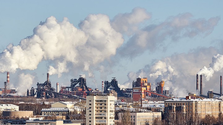 Smoke coming out of industrial buildings in a city skyline.