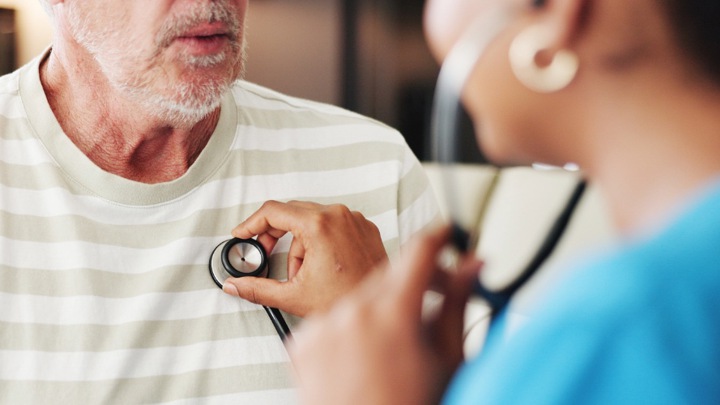 A doctor listening to the heartbeat of a male patient.