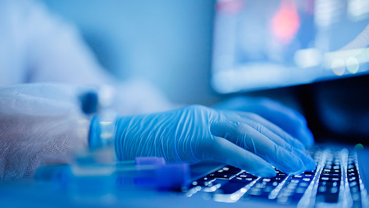 Close up of hands wearing blue gloves typing on a keyboard.
