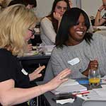 Two women working together at a table in a classroom environment and smiling. 