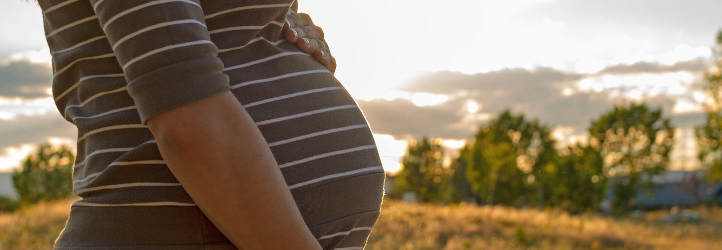 A pregnant woman standing outside in a nature setting.