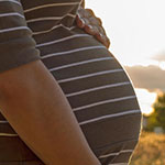 A pregnant woman standing outside in a nature setting.