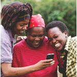 Three Black women smiling at a mobile phone screen.