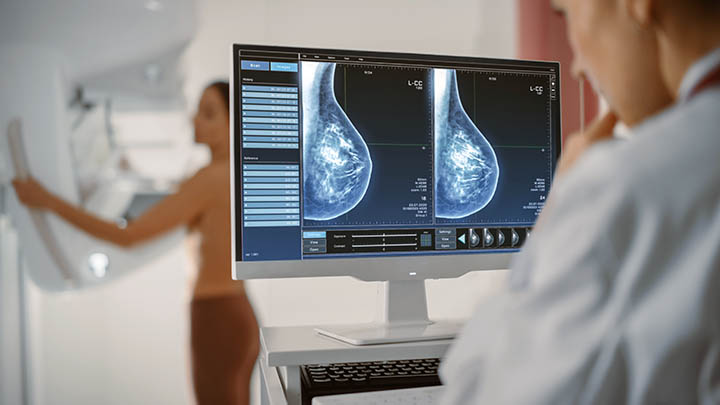 A mammographer studies tissue of a woman undergoing a mammogram.