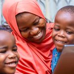 An African woman and two young boys smiling at a tablet screen.