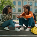 Two Black people sitting and talking on steps.