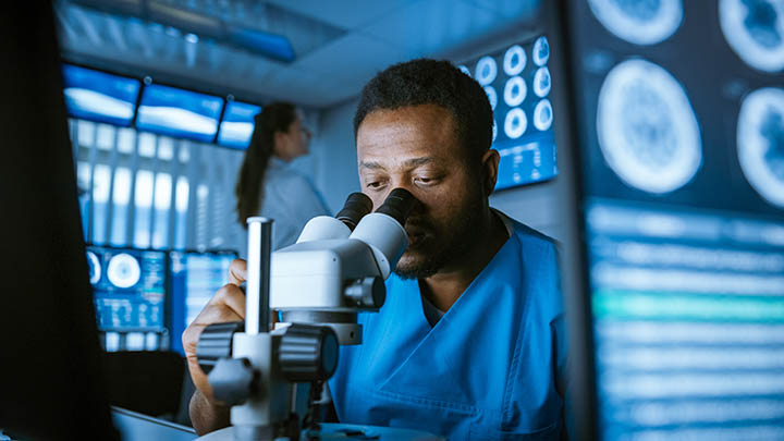 A researcher studies a biopsy under the microscope.