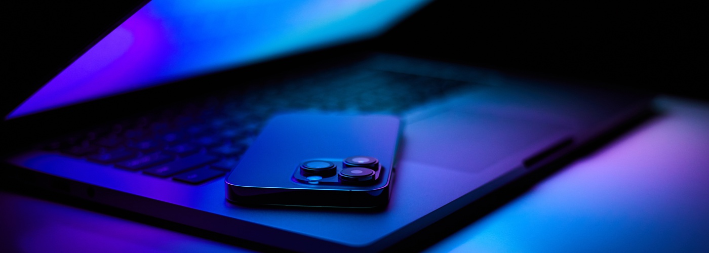 A smartphone on a laptop keyboard, bathed in blue light.