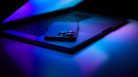 A smartphone on a laptop keyboard, bathed in blue light.