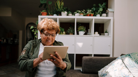 An older Black woman using an iPad at home.