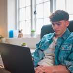 A teenage boy looking at a laptop.