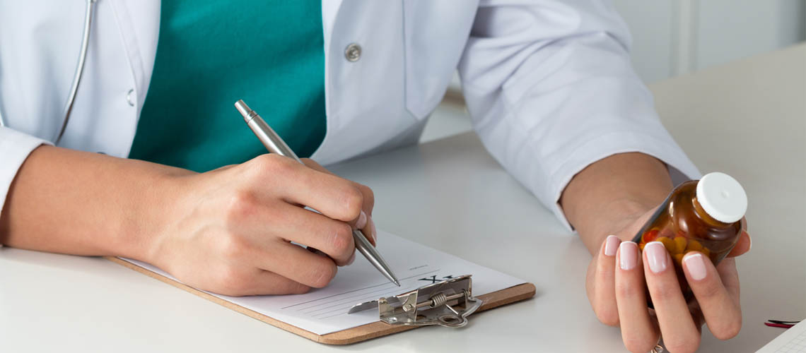Close-up view of female doctor hand holding bottle with pills and writing prescription. Healthcare, medical and pharmacy concept.
