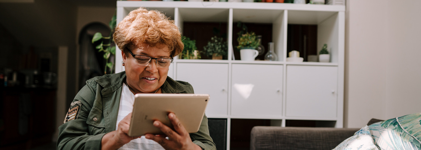 An older Black woman using an iPad at home.