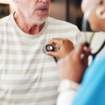 A doctor listening to the heartbeat of a male patient.
