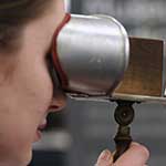 A young woman, close-up, looking through a wooden stereoscopic viewer.