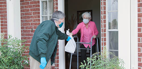 An elderly person receives shopping bag from a helper wearing a face mask.