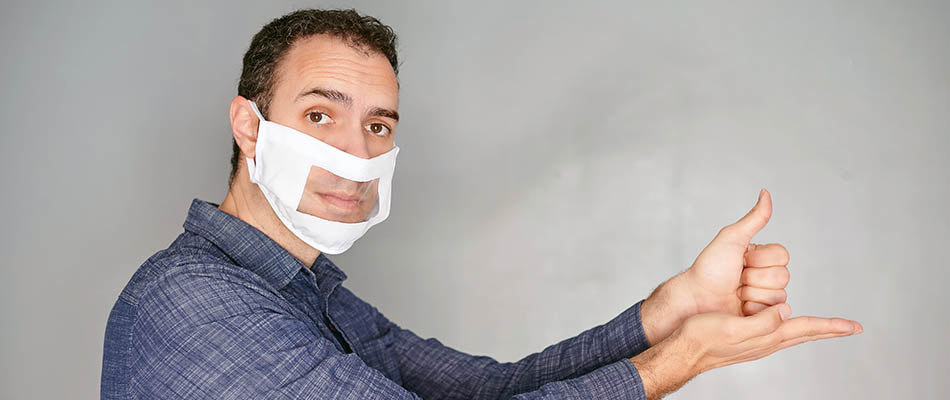 A man wearing a face mask with a window, while giving the sign for help.