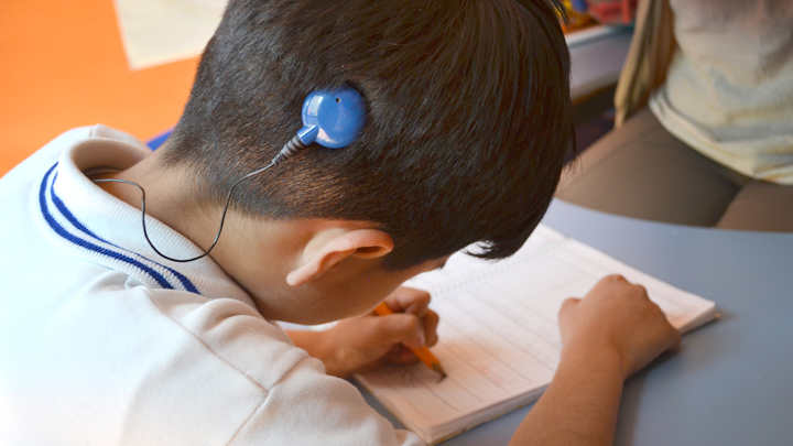 A photo of a deaf child writing at a school desk.
