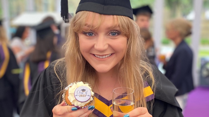 Hannah in her graduation gown holding a cupcake with the words 'Class of 2023' on it.