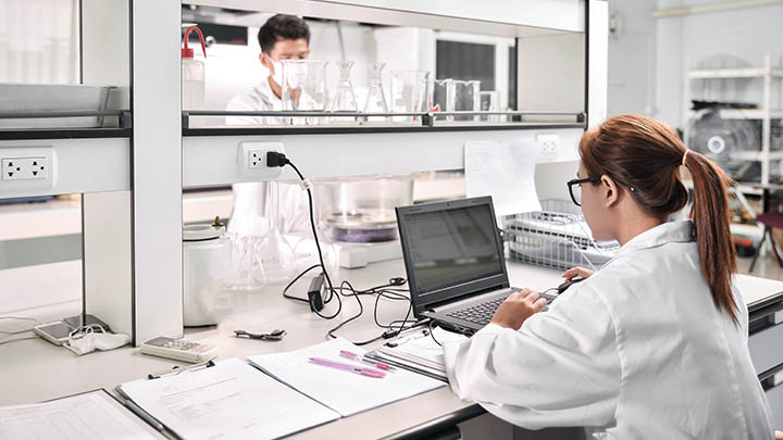 A researcher typing on a laptop at a lab bench.