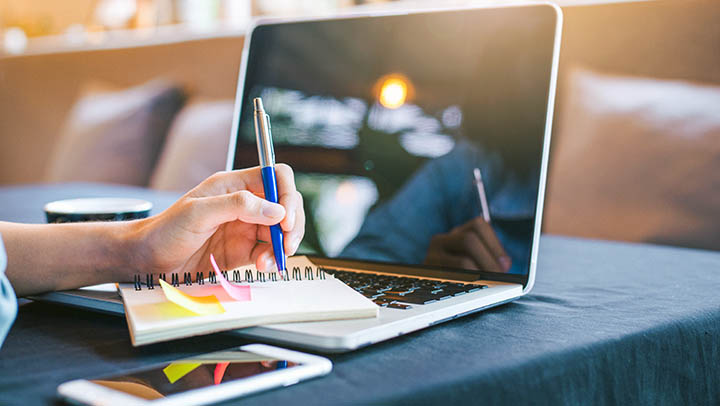 A student making notes while referring to a computer.