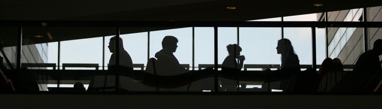 Silhouette of people sitting at tables by a large window.
