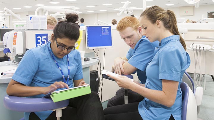Three dentistry students looking at a tablet in the simulation suite.