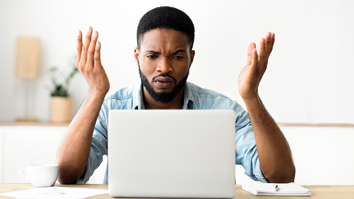 A person throwing his hands up in the air in frustration at technical issues on a laptop.
