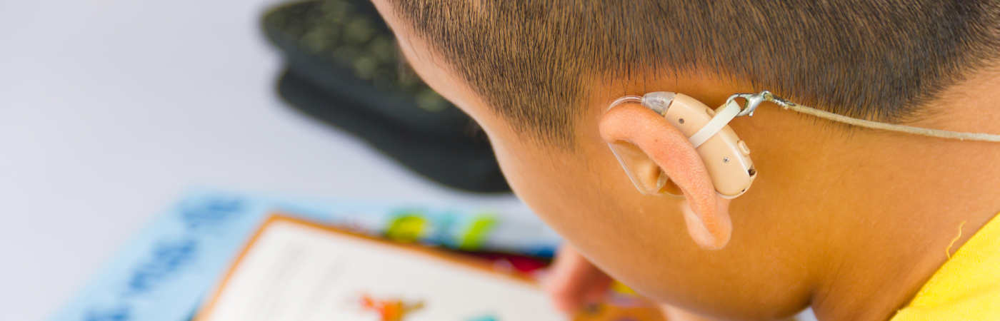 A child wearing a hearing aid studying a book.