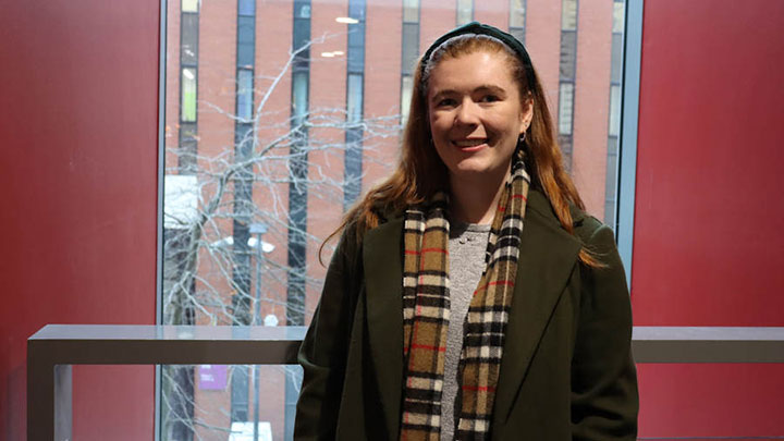 Student Catriona smiling towards the camera, standing in front of a large window. 