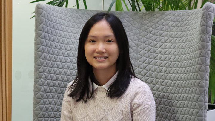Yibe a medical student at Manchester, smiling towards the camera whilst sitting on a grey chair.