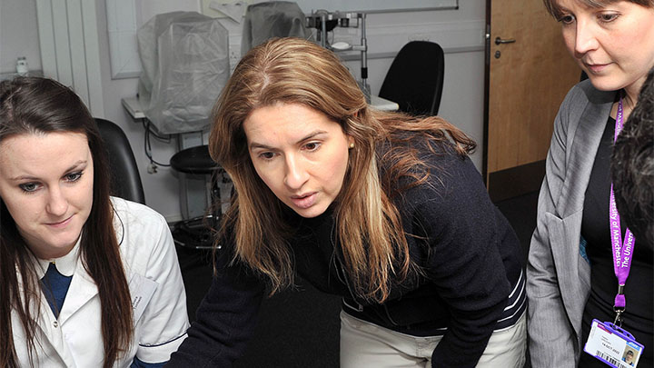 Two optometry students and their lecturer looking at a computer monitor.