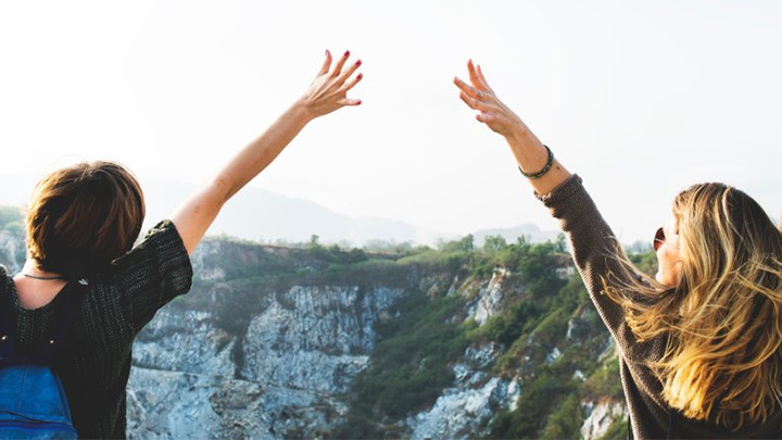 Students with raised hands, celebrating against countryside backdrop.