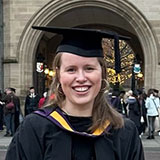 A portrait image of a smiling lady wearing graduation robes in front of a stone arch at The University of Manchester.