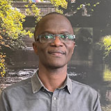 A portrait image of a man wearing a green shirt, with an image of a garden behind him.