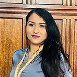 A portrait image of a smiling lady wearing a light blue top against a wooden panel background.